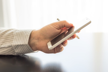 A man is holding a white cellphone and stylus in his hand.