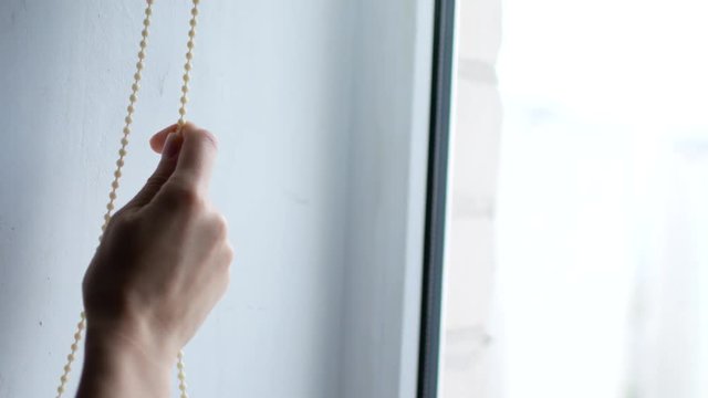 A woman's hand opens the blinds on the window