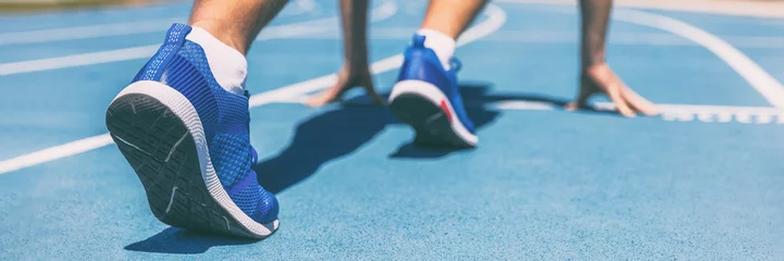 Foto op Plexiglas Sprinter die op de start van de race wacht op atletiekbanen in het openluchtstadion. Sport en fitness runner man atleet op blauwe piste met hardloopschoenen. Bannerpanorama. © Maridav