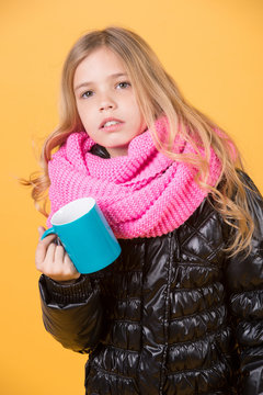 Child hold mug in black jacket and pink scarf