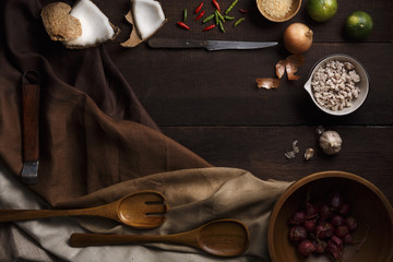 Thai food cooking ingredients with garlic, lemon, coconut, sugar, pork, chilli, wooden spoon and folk and knife on wooden board background. Top view with copy space in center