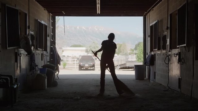 Wide slow motion silhouette of girl cleaning floor of stable / Lehi, Utah, United States