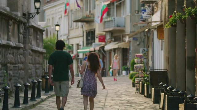 Wide slow motion panning shot of couple walking on cobblestone street / Veliko Tarnovo, Bulgaria