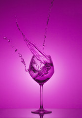 Water splash in out of glass. Water splashing out of a tall wine glass. Pink gradient background. Reflection.