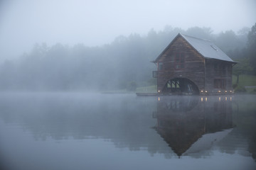 Symmetry view of log cabin by lake against trees during foggy weather