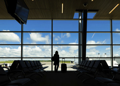 Silhouette woman with suitcase standing against window at airport