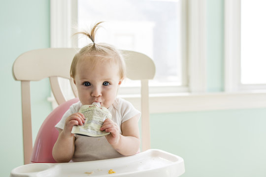 Portrait Of Baby Girl Eating Apple Sauce From Pack At Home