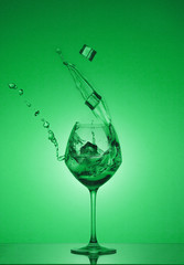 Ice cubes fall into a glass and water is poured out. Water splashing out of a tall wine glass. Gradient background and reflection.