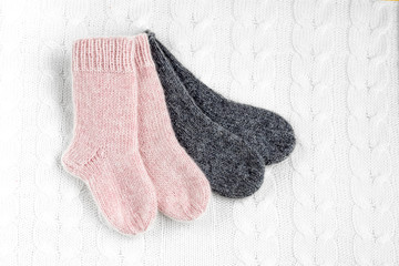 A pair of cute small different colored cashmere knitted newborn baby socks on a white woolen background