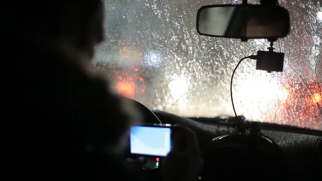 A man gets into the car and turns on the navigator on the smartphone