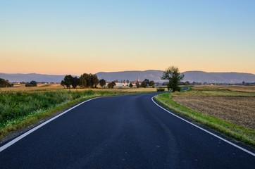 Summer rural landscape. Asphalt road with mountains and village in the background.