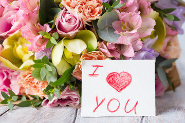 Pastel flowers bunch on a wooden light background with tag. I love you. Selective focus....