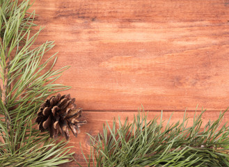 Frame made of fir branches and bumps on a wooden background.