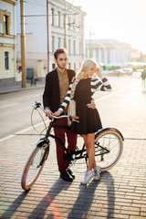 Obraz na płótnie Canvas Beautiful stylish vintage hipster couple in love posing on the street in summer evening together with bicycle