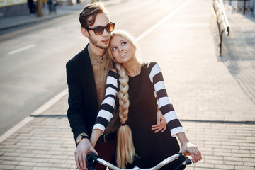 Beautiful stylish vintage hipster couple in love posing on the street in summer evening together with bicycle