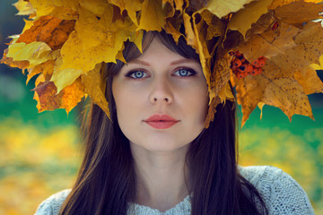 Naklejka na ściany i meble portrait of a young girl with a wreath of leaves on her head in an autumn park in moscow, russia
