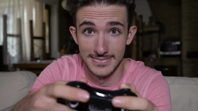 Smiling captivated teenager with game controller having fun playing video game sitting on couch at home in slow motion