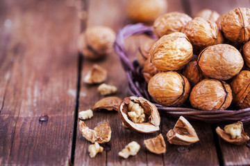 Fototapeta na wymiar Whole walnuts in basket on rustic old wooden table