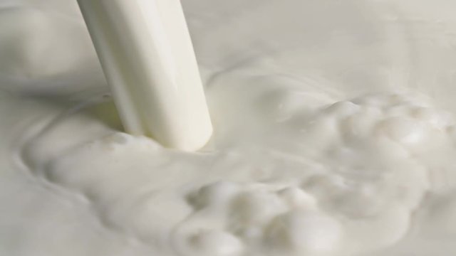 Milk pouring to liquid white surface full hd slow-motion extreme close-up video nature background with copy space. Milk falling splashing and bubbles. Dairy breakfast