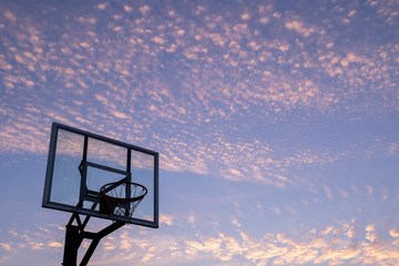 Silhouette of outdoor basketball goal with clear backboard and sunset in the background