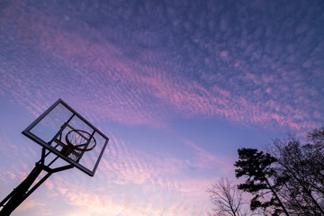 Silhouette of outdoor basketball goal with clear backboard and sunset in the background