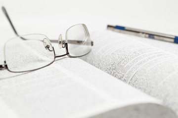 Reading glasses and pen on a book with a white background 