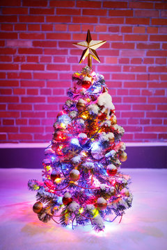 Christmas tree with festive lights in snow outdoors, purple brick wall background