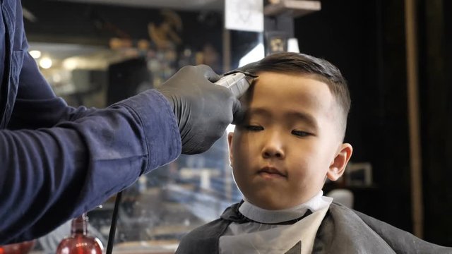 Barber in black gloves gently shaves bangs Asian child 60 fps