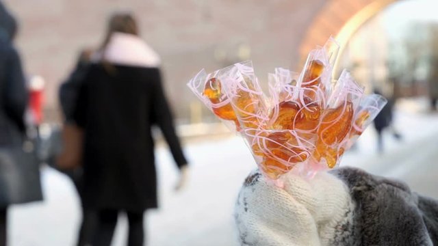 Senior adult woman selling homemade sugar lollipops in individual packaging in the in sunny winter day street while passers going by sidewalk