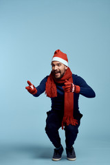 Obraz premium man in full growth sits, light blue background, free space for copy, Christmas hat, holiday, christmas