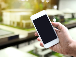 Hand holding smartphone over blurred background of house model samples