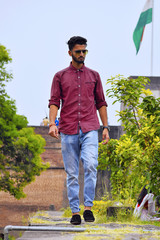 Young man with checked shirt walking. Indian flag in background, Pune, Maharashtra. - obrazy, fototapety, plakaty