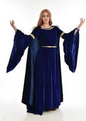 full length portrait of girl wearing long blue velvet gown and fur lined cloak, standing pose  on white background.