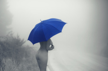 Black and white picture of young  naked female with blue umbrella on the road in the fog. Artistic...