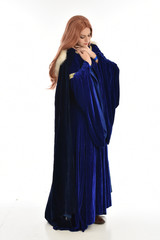 Naklejka premium full length portrait of girl wearing long blue velvet gown and fur lined cloak, standing pose on white background.