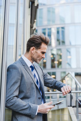 Fototapeta premium businessman leans against an office building and watches the time