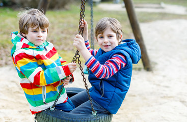 Two little kid boys having fun with chain swing on outdoor playground