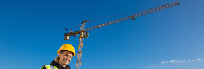 panoramic view of young female construction worker with hardhat , crane in background.