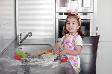 Little girl is cooking on kitchen. Having fun while making cakes and cookies.