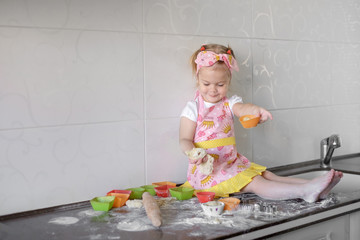 Little girl is cooking on kitchen. Having fun while making cakes and cookies.