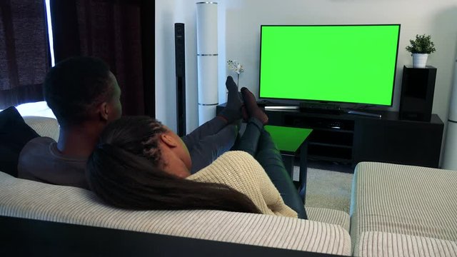 Young black couple in love watch television in living room- man switches program