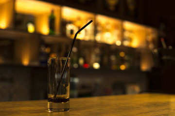 A glass of collins with black straw and a non-drunk beverage on the bar counter