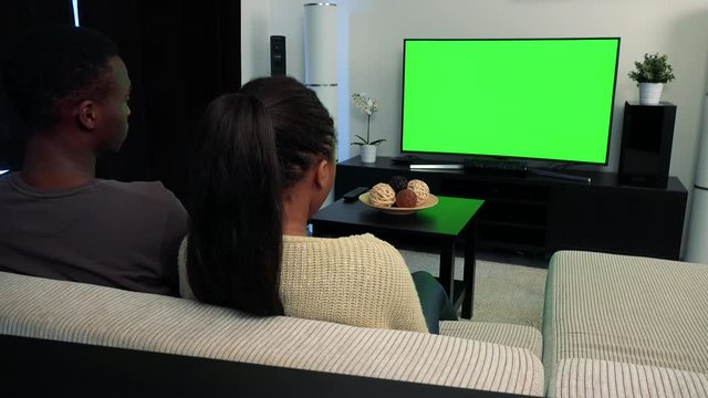 Young black couple watch television in living room and then they agree to camera