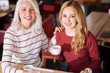 Lovely evening. Positive emotional senior woman looking happy and relaxed while sitting at the table in a cafe with her dear kind granddaughter
