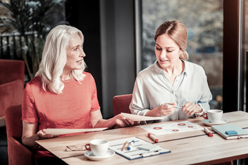 Busy women. Cheerful clever friendly designers sitting in a cafe and discussing their new exciting project with color schemes and graphics being on the table in front of them