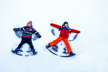 Fototapeta na wymiar Two little siblings kid boys in colorful winter clothes making snow angel, laying down on snow.