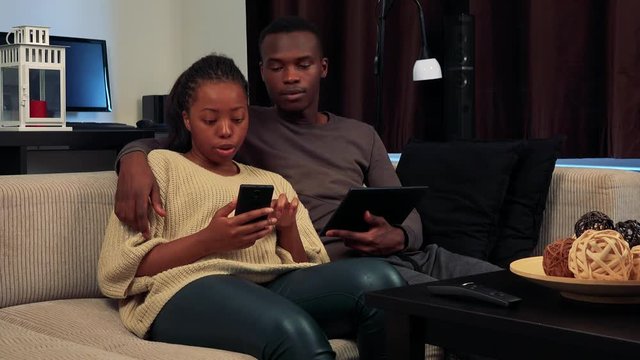 Young Black Couple Work On Smartphone And Tablet In Living Room