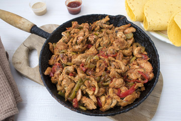 Chicken stew with red and green pepper, with red onion, pickled cucumber and spices in a frying pan.