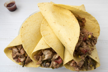 Fajitas consisting of chicken stew with red and green pepper, with red onion, pickled cucumber and spices wrapped in a corn cake.