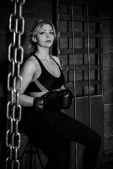 Fototapeta na wymiar Woman hits the heavy bag with a strong kick. Concept about fit boxe, martial arts and sport. Simple woman in black boxing gloves. She is fighter for success.